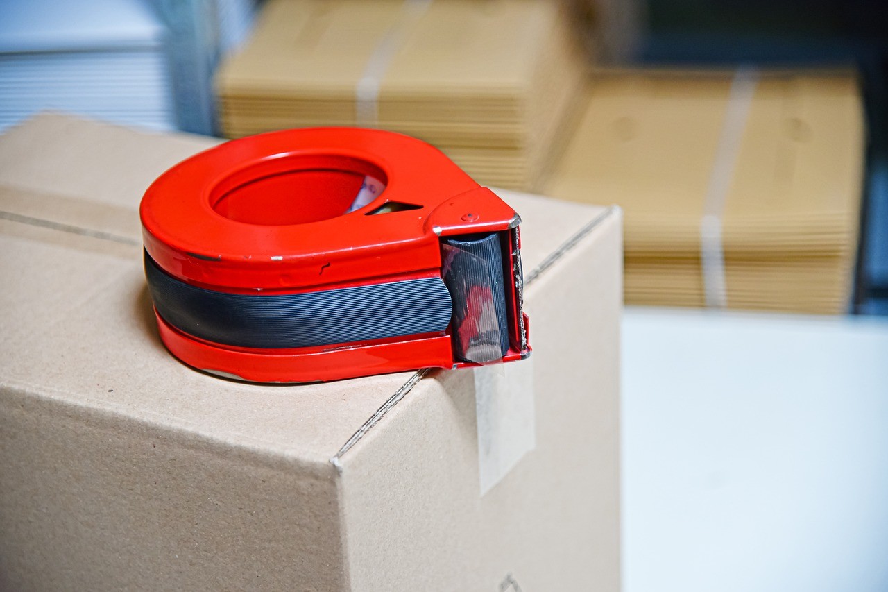 Tape for packing parcels on a sealed cardboard box, folded boxes in the background