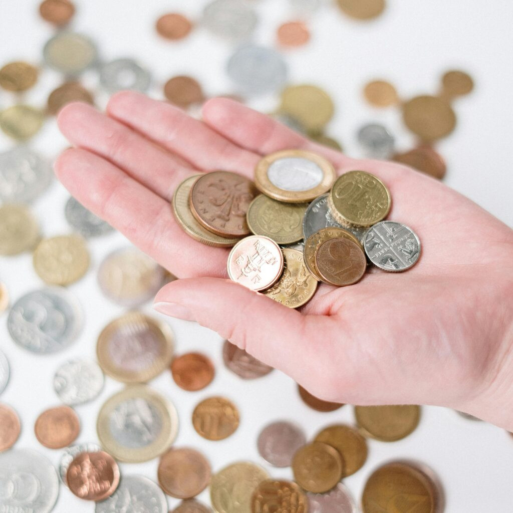 a person holding coins in their hand, with more coins underneath on a white background