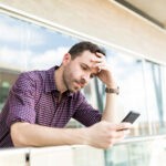 tensed-man-reading-distressing-news-smartphone-while-leaning-railing-shopping-mall.jpg