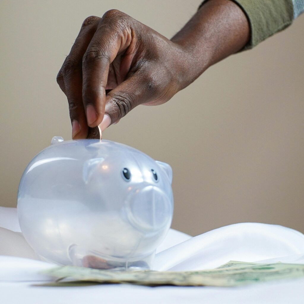 A person throwing a coin into a transparent piggy bank
