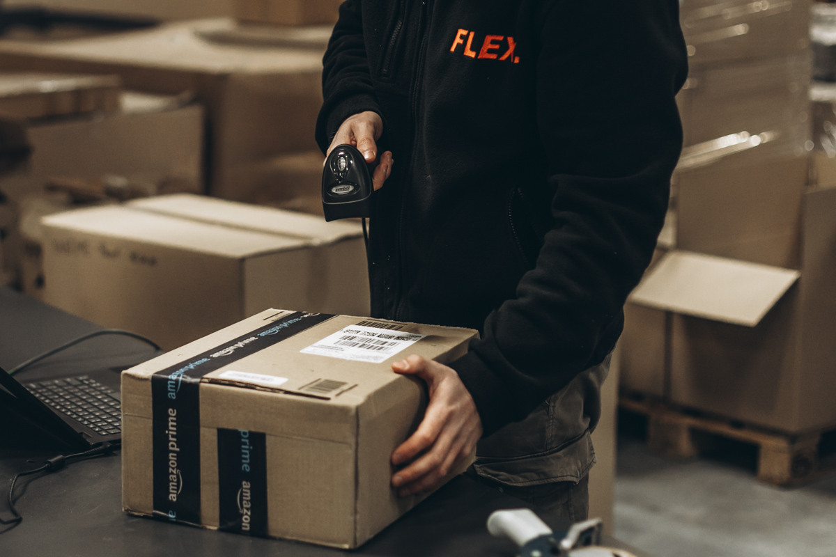 Warehouse employee scanning the shipping label on a packed parcel with a handheld barcode scanner at a fulfillment workstation.