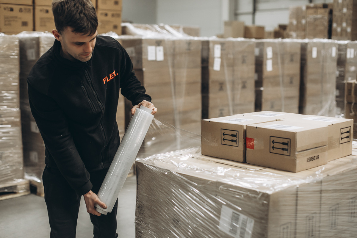 FLEX. warehouse employee wrapping a pallet of cartons with stretch film to secure goods for storage or outbound shipment.